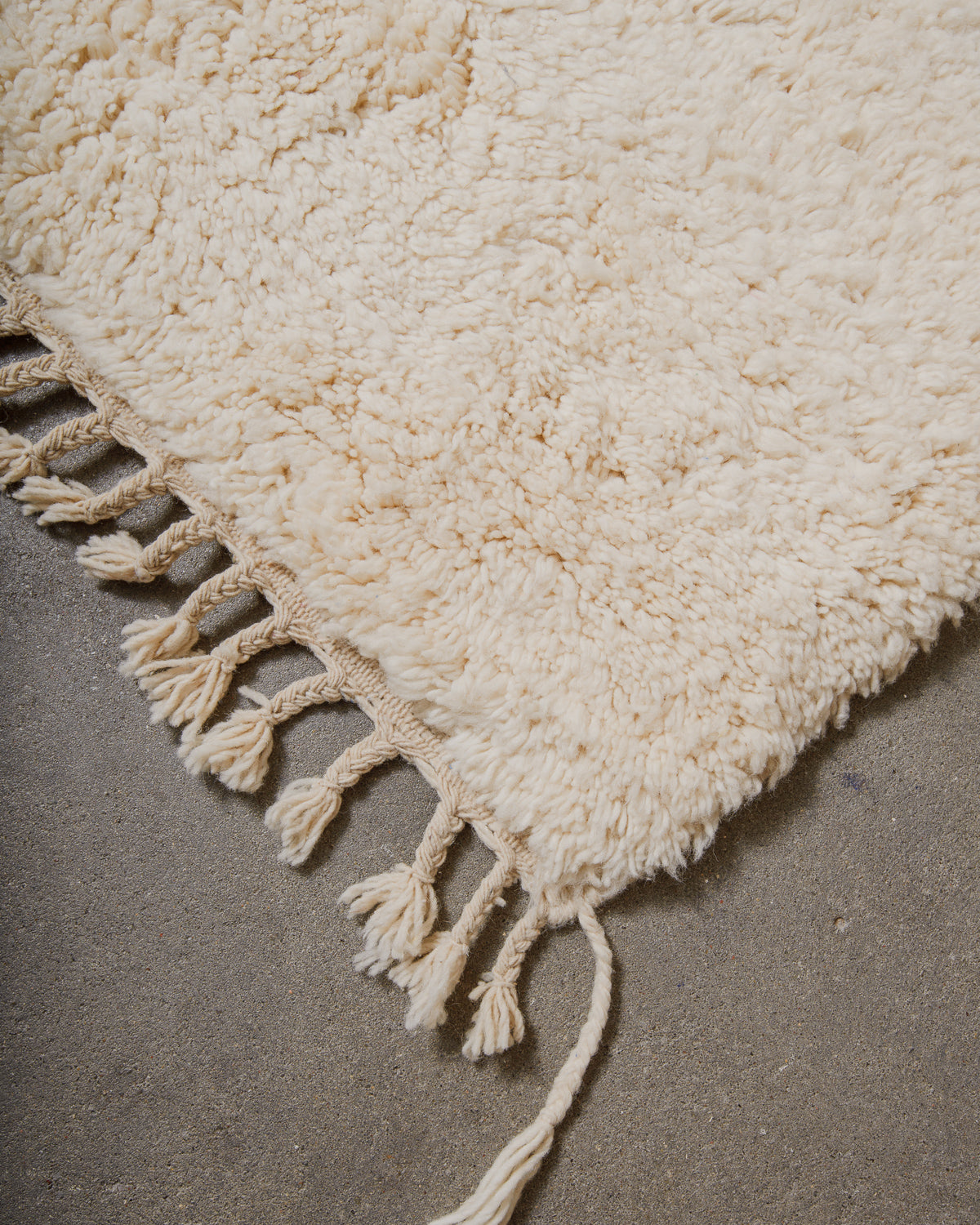 Corner or cream rug with fringes on cement floor.